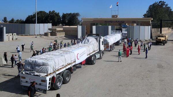 Люди на египетской стороне КПП Рафах наблюдают, как колонна грузовиков с гуманитарной помощью пересекает сектор Газа