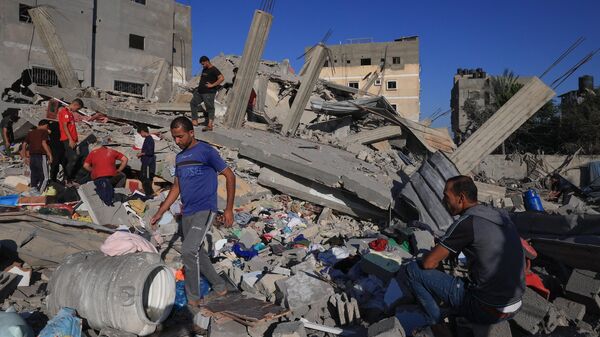 Люди на развалинах здания, разрушенного в результате израильской бомбардировки в Рафахе на юге сектора Газа