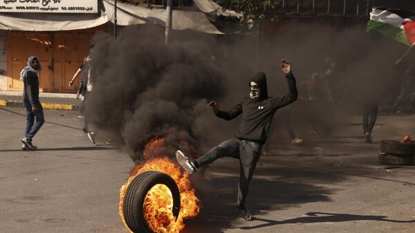 Палестинский демонстрант катит горящую шину в сторону израильских сил безопасности в оккупированном городе Хеврон на Западном Берегу реки Иордан
