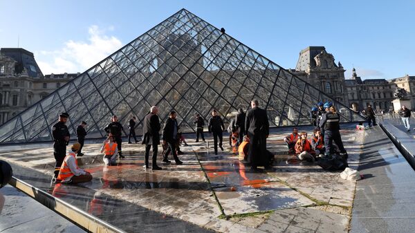 Сотрудники полиции задерживают активистов движения Derniere Renovation (Последнее обновление), обливших оранжевой краской стеклянную пирамиду Лувра