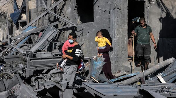 Родители с детьми у разрушенного в результате обстрела здания в секторе Газа
