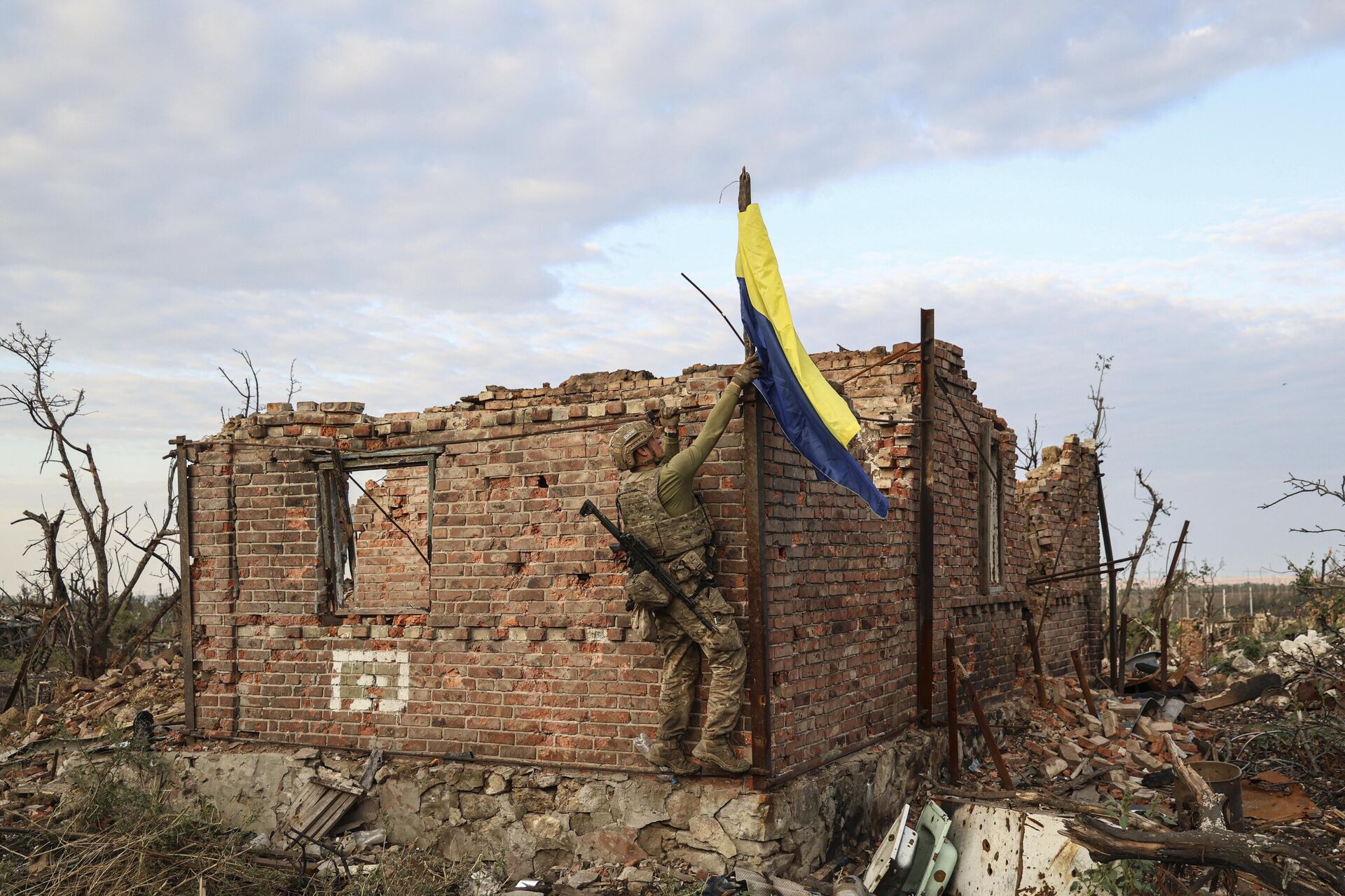 Военнослужащий подразделения ВСУ поднимает украинский флаг над ранее разрушенным зданием - РИА Новости, 1920, 22.11.2023