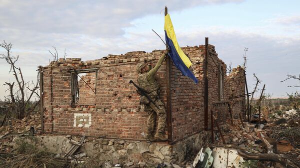 Военнослужащий подразделения ВСУ поднимает украинский флаг над ранее разрушенным зданием