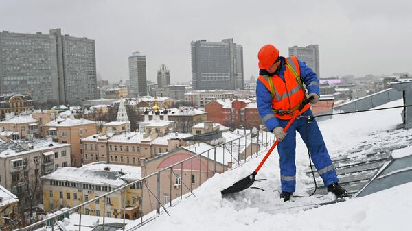 Сотрудник коммунальных служб отчищает крышу одного из домов в Москве
