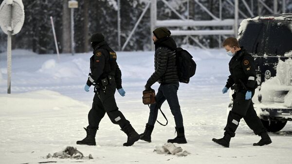 Офицеры финской пограничной службы сопровождают мигранта на КПП Райа-Йоосеппи в северной Финляндии. 26 ноября 2023 года
