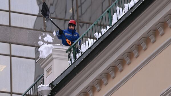 Работник коммунальной службы очищает крышу дома после снегопада в Москве