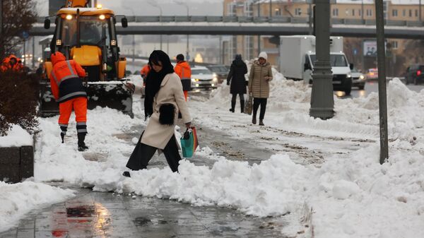 Прохожие и работники коммунальной службы на заснеженной улице после снегопада в Москве