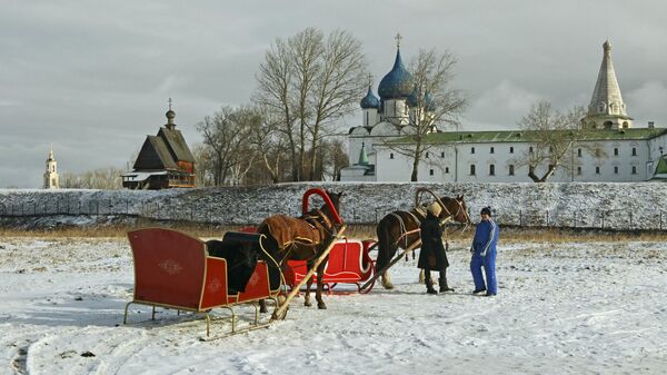 Запряженные лошадьми сани на фоне Суздальского Кремля и деревянной церкви Николая Чудотворца