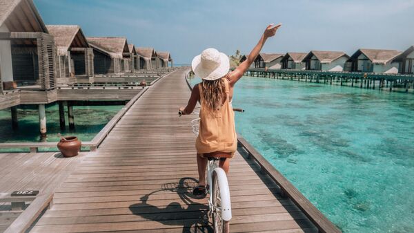 Девушка катается на велосипеде по деревянному пирсу вдоль вилл на Мальдивах