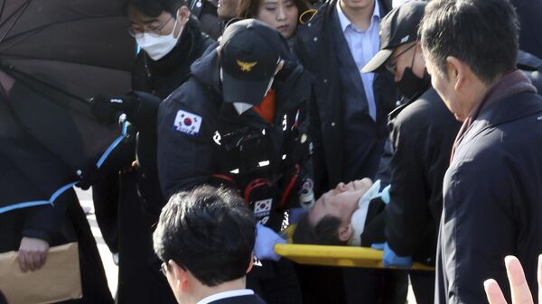 Лидера южнокорейской оппозиции Ли Джэмёна на носилках переносят спасатели в Пусане, Южная Корея. 2 января 2024