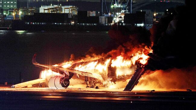 Горящий самолет Japan Airlines на взлетно-посадочной полосе токийского аэропорта Ханэда