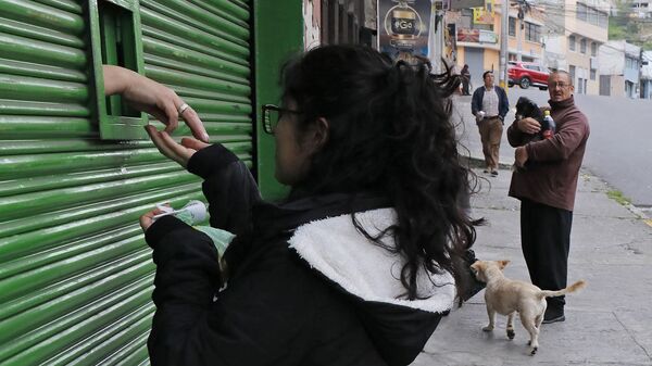 Женщина покупает товар через маленькое окошко в металлической занавеске  во время чрезвычайного положения в Кито, Эквадор