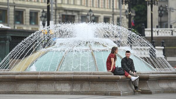 Молодые люди отдыхают возле фонтана на Манежной площади в Москве.