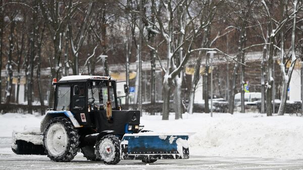 Сотрудник коммунальной службы на тракторе убирает снег