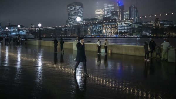 Люди гуляют вдоль набережной Темзы