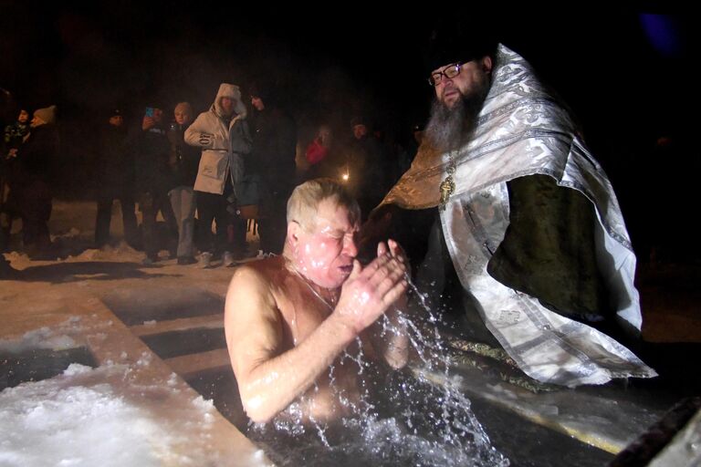 Мужчина и настоятель православного храма Святителя Луки Енисейской епархии Сергий Рыжов во время крещенских купаний на реке Верхняя Подъёмная в посёлке Большая Мурта в Красноярском крае