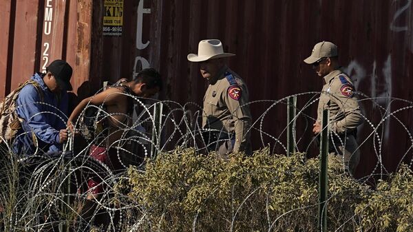 Сотрудник Департамента общественной безопасности штата Техас наблюдает за мигрантами из-за колючей проволоки на границе Техаса с Мексикой