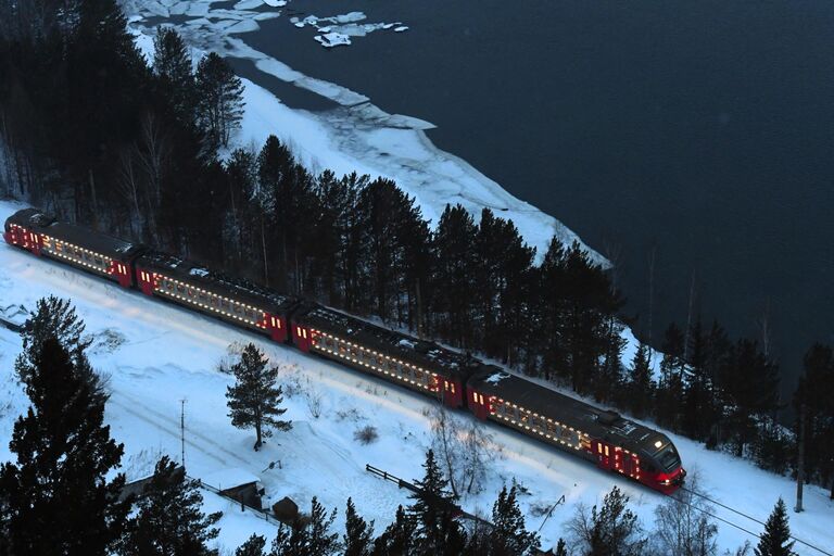 Пригородная электричка, украшенная новогодней иллюминацией, едет вдоль Енисея в Красноярском крае