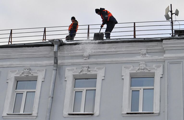 Сотрудники коммунальной службы во время уборки снега с крыши дома в Москве