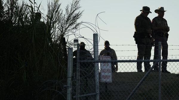 Полицейские штата Техас стоят возле знака Посторонним вход воспрещен и забора с колючей проволокой вдоль берега Рио-Гранде в парке Шелби, Игл-Пасс