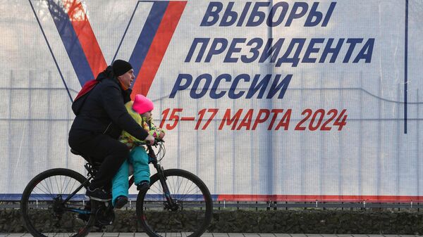 Мужчина с ребенком на велосипеде у предвыборного плаката на одной из улиц города Саки