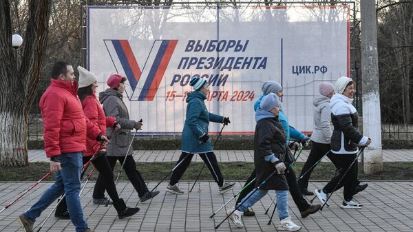 Люди занимаются скандинавской ходьбой у предвыборного плаката на одной из улиц города Саки