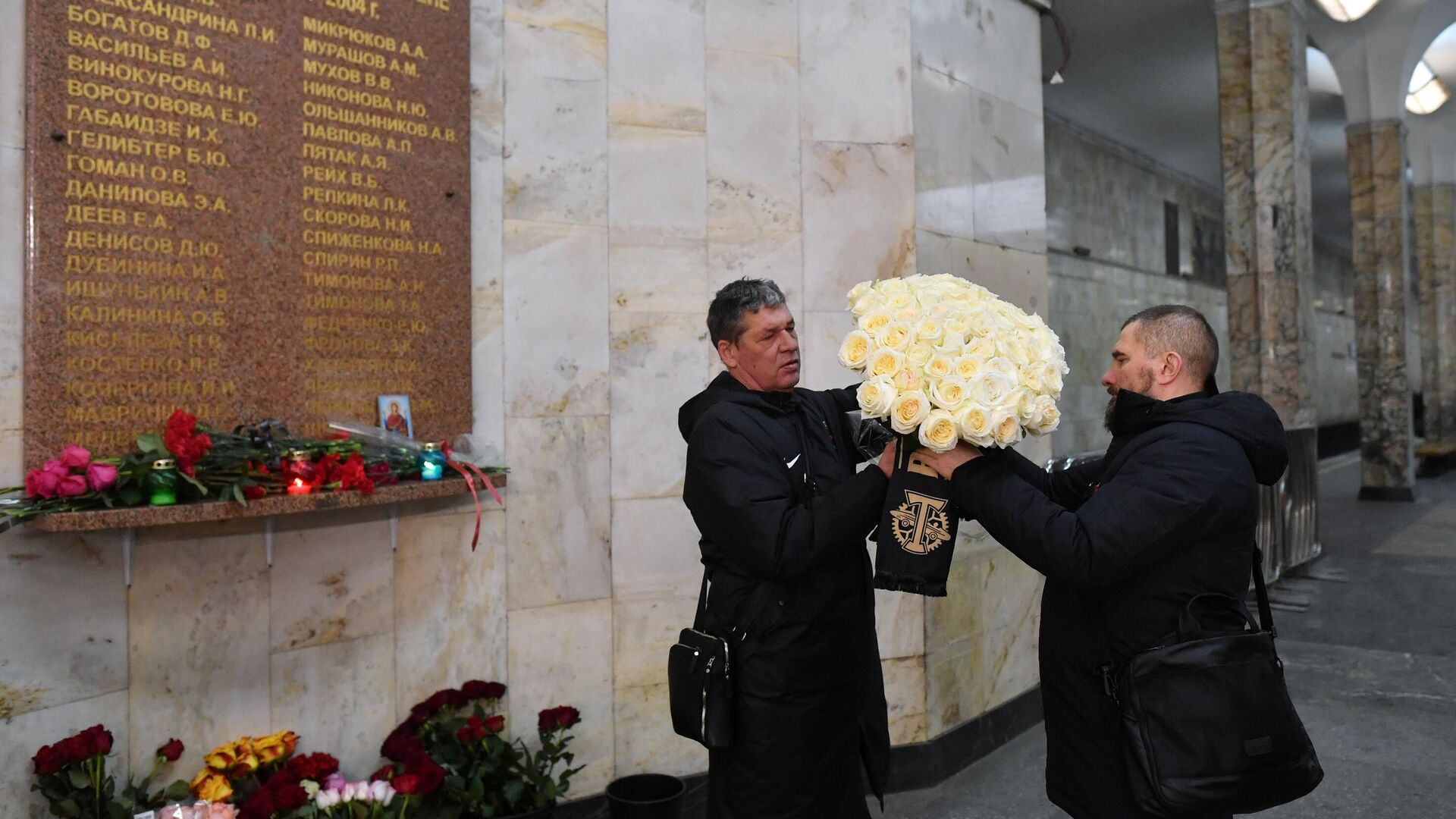 Мужчины оставляют цветы у памятной таблички со списком жертв террористического акта, размещенной на станции метро Автозаводская. 6 февраля 2024 - РИА Новости, 1920, 06.02.2024