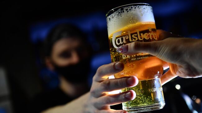 Бармен наполняет бокал пивом Carlsberg 