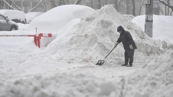 Мужчина убирает снег лопатой в одном из московских дворов