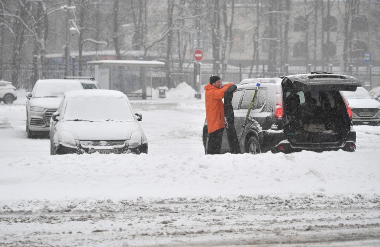 Мужчина стоит возле своей машины во время снегопада в Москве