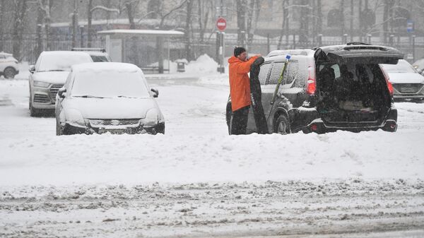 Мужчина стоит возле своей машины во время снегопада в Москве