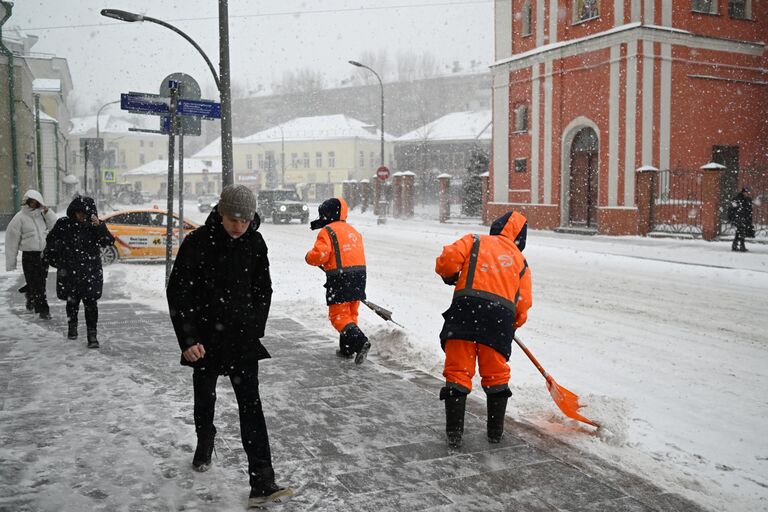 Люди переходят улицу во время снегопада в Москве