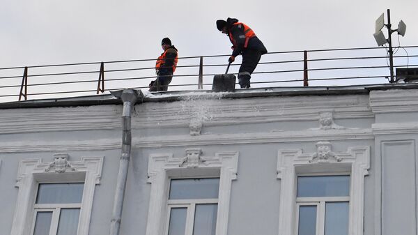 Сотрудники коммунальной службы во время уборки снега с крыши дома в Москв