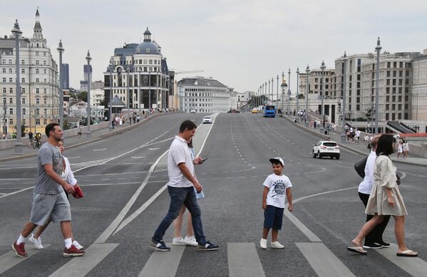 Прохожие идут по пешеходному переходу перед Большим Москворецким мостом