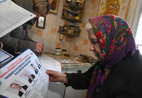 Жительница города изучает избирательный бюллетень на выездном голосовании в Северодонецке в первый день досрочного голосования на выборах президента РФ в ЛНР