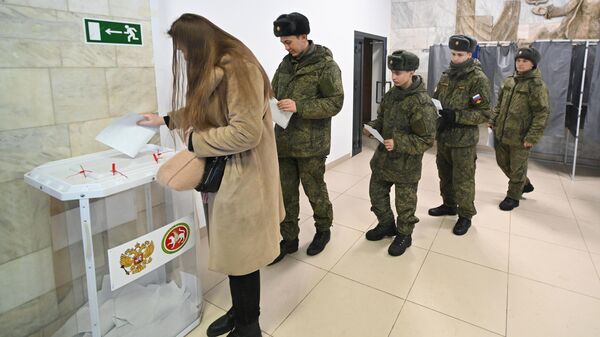 Девушка и курсанты Казанского танкового училища голосуют на выборах президента России на избирательном участке №340 в Казани