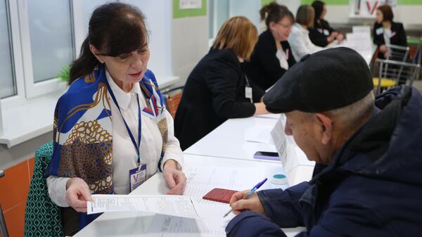 Член избирательной комиссии помогает мужчине оформить документы для голосования на выборах президента России на избирательном участке в Белгороде. 15 марта 2024