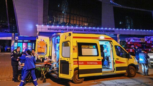 Медики грузят в машину скорой помощи раненую женщину после теракта в Крокусе