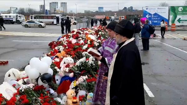 Панихида по погибшим у стихийного мемориала с цветами рядом с Крокус сити холлом