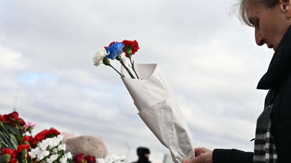 Женщина возлагает цветы в цветах российского флага на стихийном мемориале у здания концертного зала Крокус Сити Холл, где произошел теракт