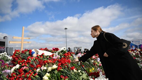 Девушка возлагает цветы на стихийном мемориале у здания концертного зала Крокус Сити Холл, где произошел теракт