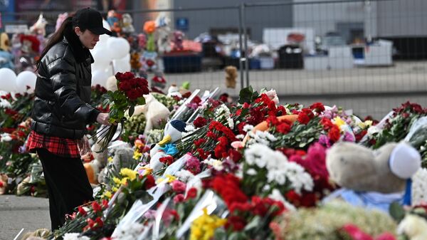 Женщина возлагает цветы у стихийного мемориала у здания концертного зала Крокус Сити Холл, где произошел теракт