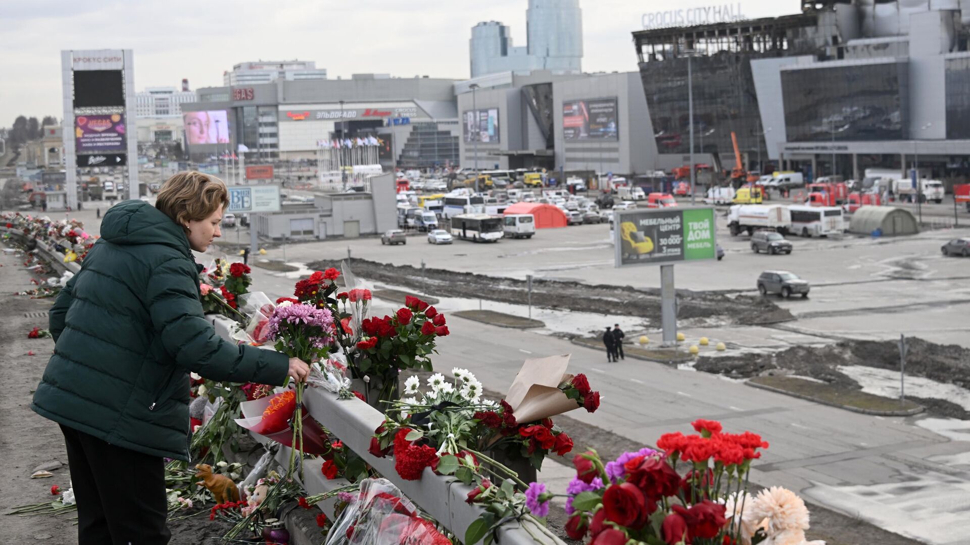 Женщина возлагает цветы у стихийного мемориала вдоль дороги у здания концертного зала Крокус Сити Холл, где произошел теракт - РИА Новости, 1920, 03.04.2024