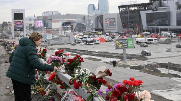 Женщина возлагает цветы у стихийного мемориала вдоль дороги у здания концертного зала Крокус Сити Холл, где произошел теракт