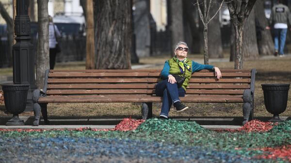 Женщина отдыхает на скамейке во время теплой погоды в одном из парков Москвы