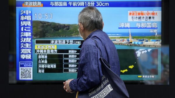 Мужчина у экрана с новостями о цунами в регионе Окинавы и землетрясении вблизи Тайваня