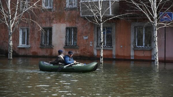 Мужчины передвигаются на надувной лодке на одной из подтопленных улиц в Орске