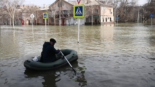 Мужчина передвигается на надувной лодке на одной из подтопленных улиц в Орске