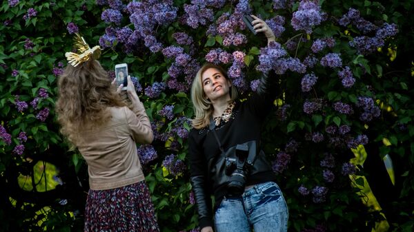 Девушки фотографируются возле сирени в Сиреневом саду в Москве
