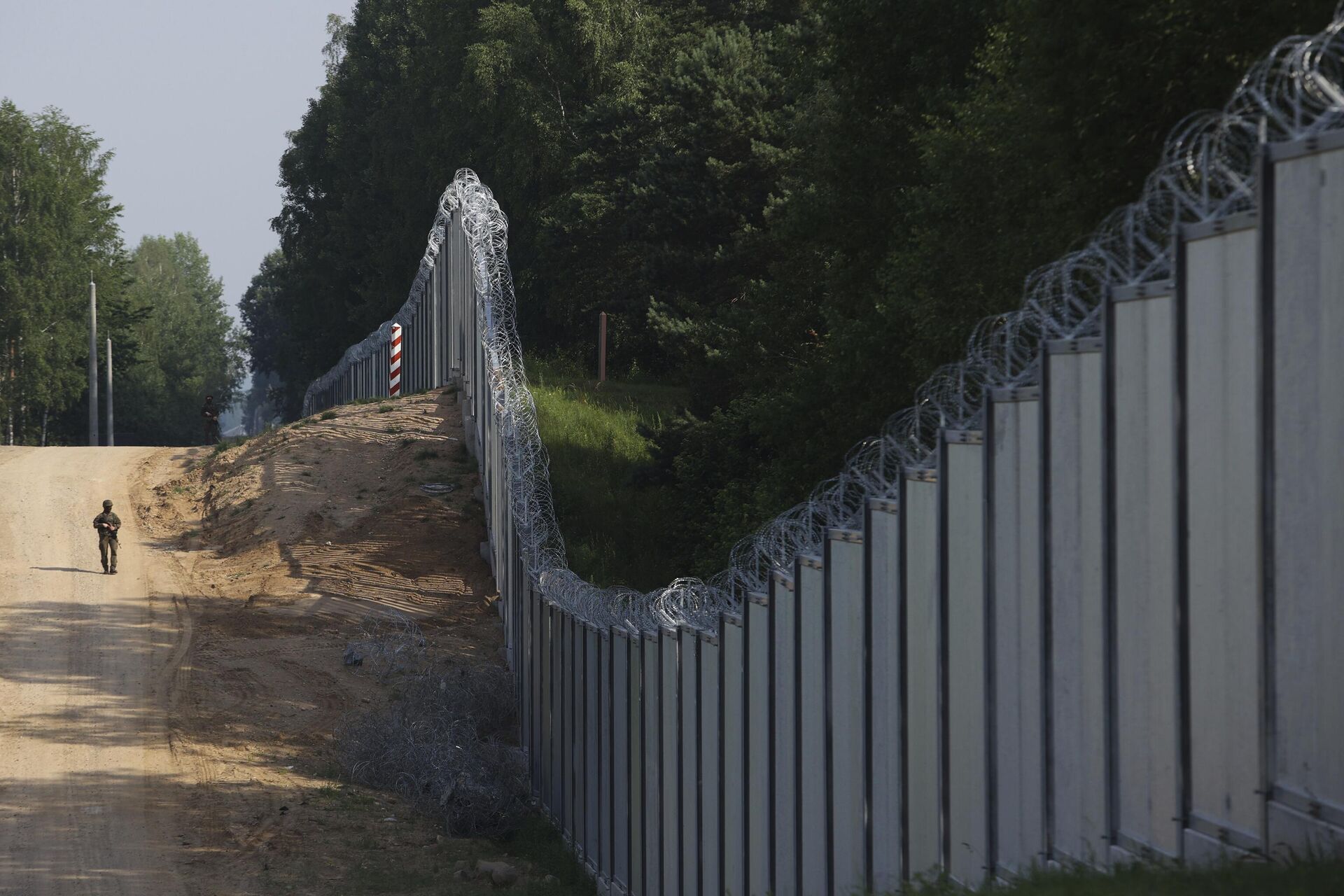 Польский пограничник идет вдоль металлического забора на границе Польши и Белоруссии - РИА Новости, 1920, 05.06.2024